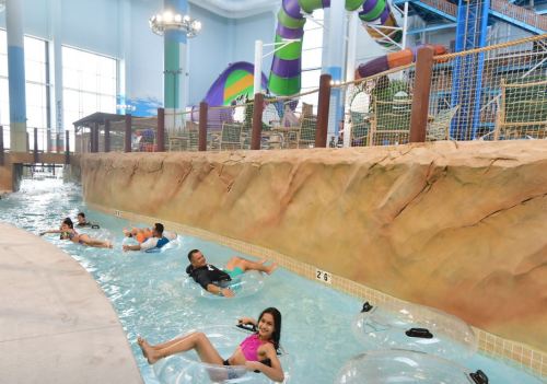 A vibrant indoor water park with a lazy river, water slides, and people floating on tubes.