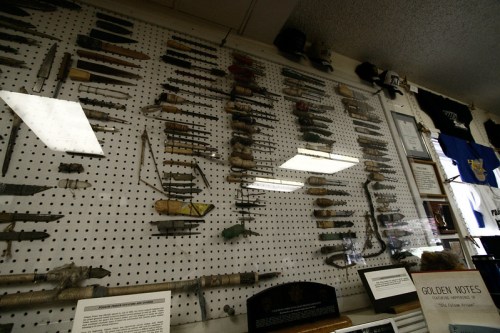 A display of various tools and artifacts mounted on a wall, with informational plaques and clothing in the background.