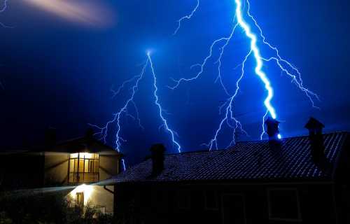 A dramatic night scene with bright lightning striking over a house, illuminating the dark sky.