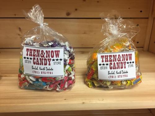 Two bags of assorted candies displayed on a wooden shelf, labeled "Then & Now Candy Store, Bismarck, North Dakota."