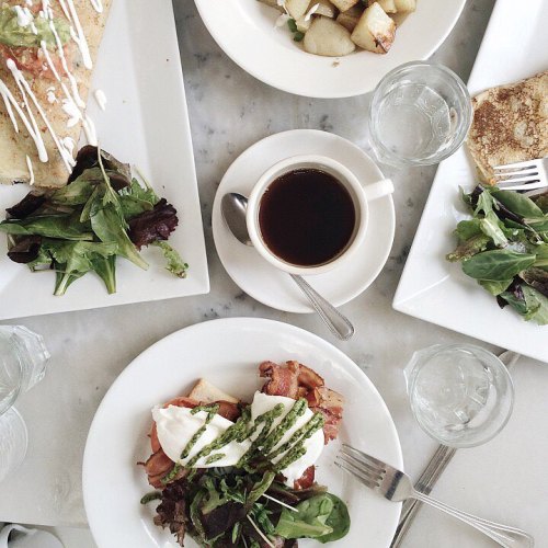 A top-down view of a brunch spread with eggs, salad, potatoes, a crepe, and coffee on a marble table.