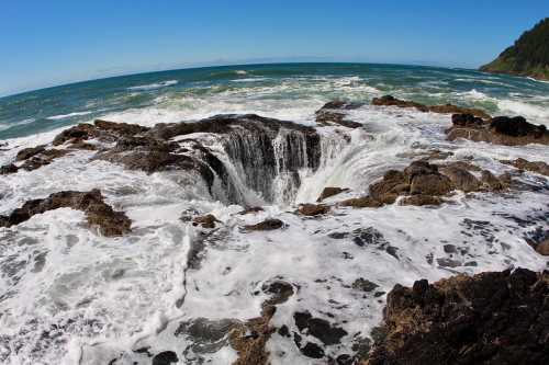 A rocky coastline with a large, circular hole surrounded by crashing waves and a clear blue sky.