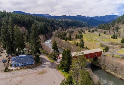 Aerial view of a red covered bridge over a river, surrounded by lush green trees and mountains in the background.