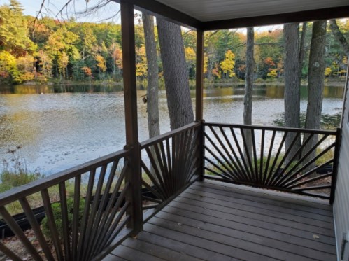 A wooden porch overlooks a serene lake surrounded by trees with autumn foliage.