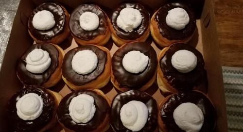 A box of chocolate-covered donuts topped with whipped cream swirls.