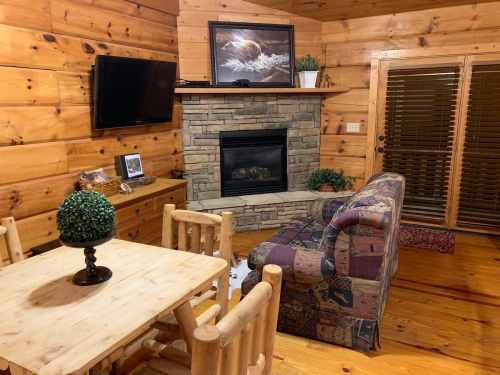 Cozy cabin interior featuring a stone fireplace, wooden furniture, and a comfortable couch. Warm, rustic decor.