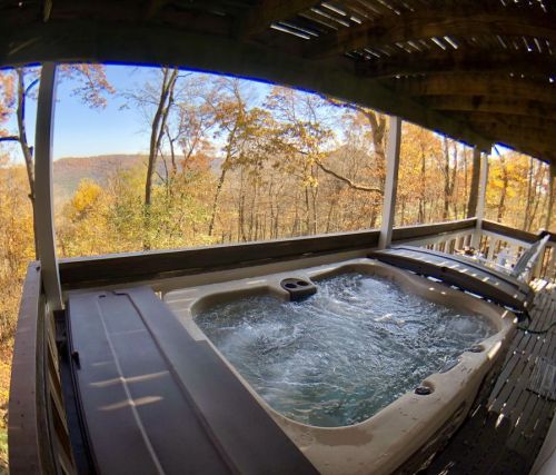 A hot tub on a wooden deck overlooking a scenic view of autumn trees and hills.