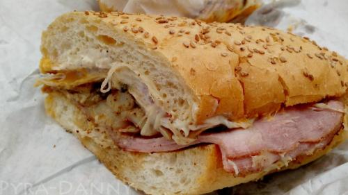 Close-up of a sesame seed sandwich filled with layers of ham and melted cheese on a soft bread roll.