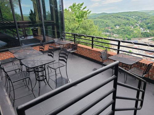 A patio with black metal tables and chairs overlooks a green landscape and distant hills.