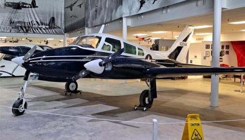 A vintage aircraft displayed in a museum, featuring a sleek blue and white design with caution signage nearby.