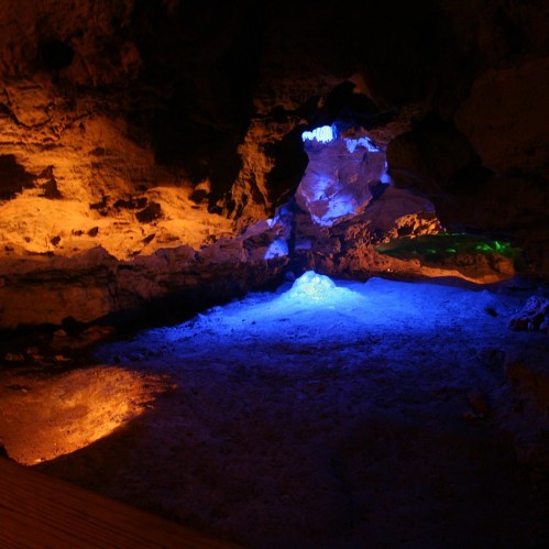 A dimly lit cave with colorful blue, orange, and green lights illuminating the rocky walls and floor.