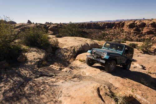 A blue Jeep navigating rocky terrain in a desert landscape under a clear sky.