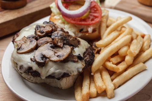 A juicy burger topped with melted cheese and mushrooms, served with crispy fries and a side of fresh vegetables.