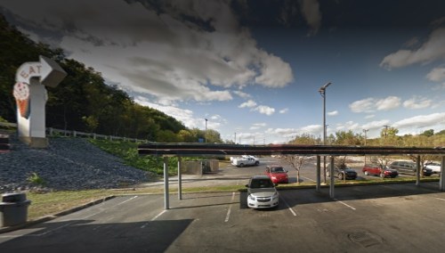 A parking lot with a covered area, surrounded by trees and a cloudy sky, featuring a basketball hoop sign.