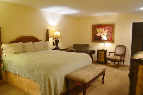 Cozy bedroom with a large bed, armchair, and decorative lamps, featuring warm colors and elegant furnishings.