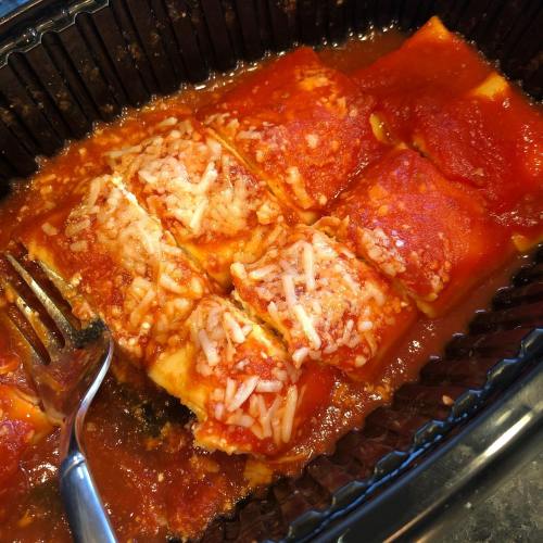 A close-up of a dish of cheesy lasagna in marinara sauce, with a fork resting beside it.