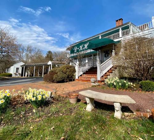 A charming building with a green awning, surrounded by blooming flowers and trees under a clear blue sky.