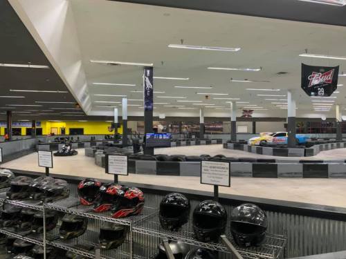 Indoor go-kart track with helmets in the foreground and karts racing on a winding track in the background.