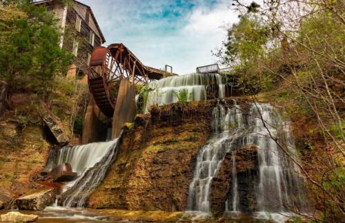 A scenic waterfall cascading over rocks, with a historic waterwheel and lush greenery in the background.