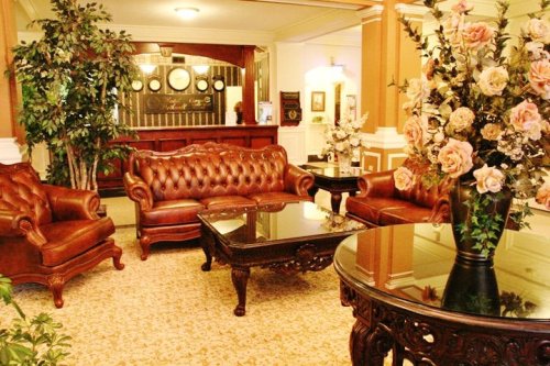 Elegant lobby with leather sofas, a glass coffee table, floral arrangements, and a reception desk in the background.