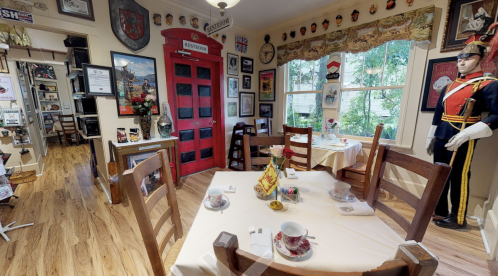 Cozy dining room with tables set for tea, vintage decor, and a red phone booth in a charming, inviting atmosphere.
