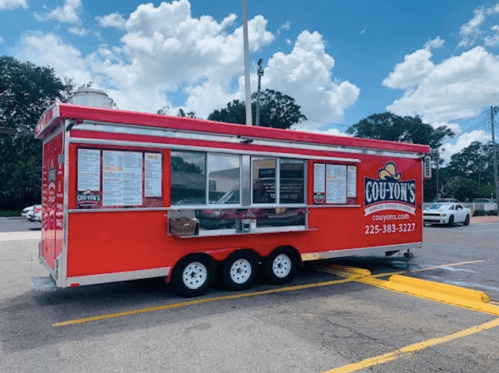 A bright red food truck with a menu displayed, parked in a lot under a blue sky with fluffy clouds.