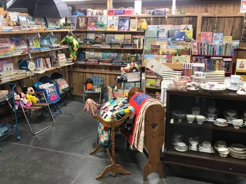 A cozy bookstore corner filled with shelves of books, toys, and vintage items, including quilts and teacups.