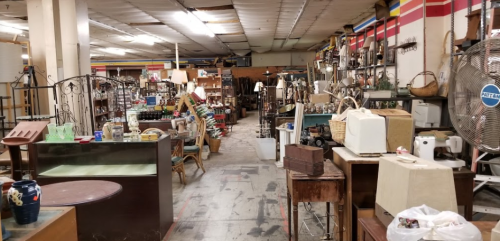 A cluttered antique store aisle filled with various furniture, lamps, and decorative items.