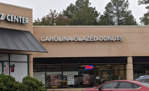 Sign for "Carolina Glazed Donuts" on a storefront, with an "Open" sign visible in the window.