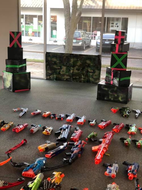 A room with camouflage decorations, two stacked boxes, and various toy guns scattered on the floor.