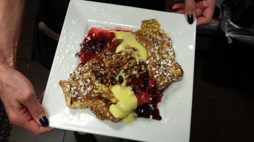 A plate of dessert featuring crispy pancakes topped with berries, custard, and a sprinkle of powdered sugar.