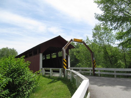 A red covered bridge with a sign, surrounded by greenery and a clear blue sky.