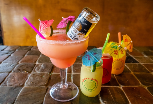 A colorful assortment of cocktails with umbrellas, including a large margarita topped with a beer bottle.