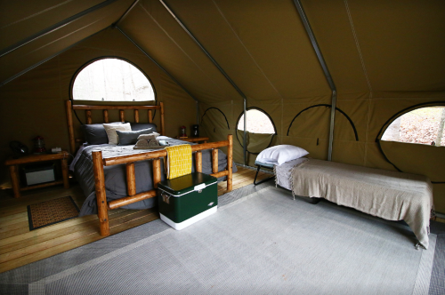 Cozy glamping tent interior with a double bed, single bed, and rustic decor, featuring large round windows.