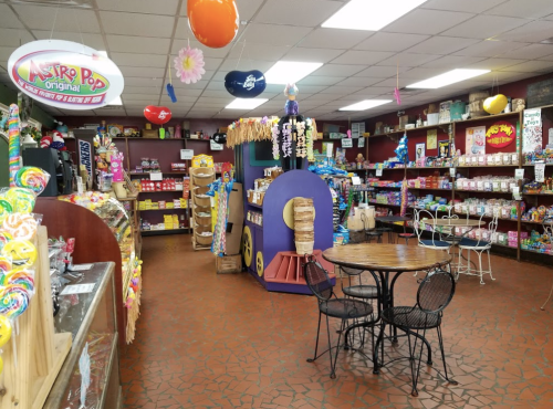A colorful candy shop interior with shelves of sweets, a round table, and decorative balloons hanging from the ceiling.