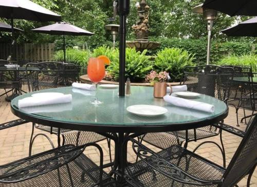 A patio dining area with a glass table, a cocktail, and lush greenery in the background.