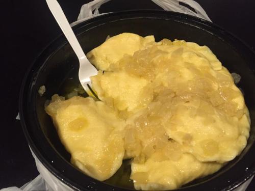 A container of dumplings topped with a yellow sauce and chopped onions, served with a plastic fork.