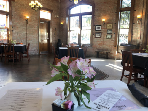 A cozy restaurant interior with wooden tables, brick walls, and a vase of flowers on a table.