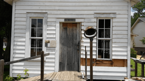 A weathered white wooden building with a door, windows, and a large horn mounted on the side.