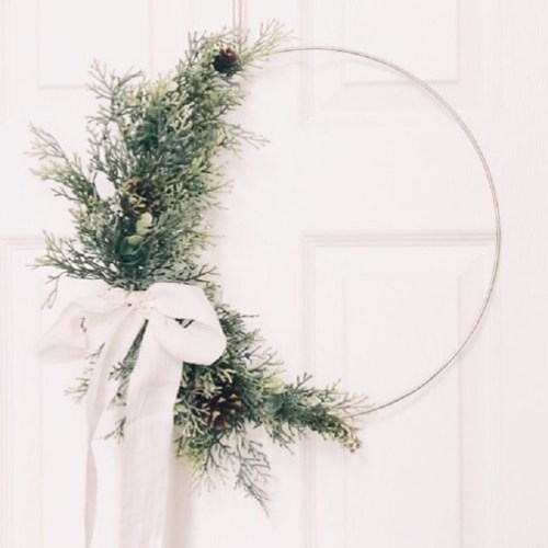 A minimalist wreath made of greenery and pinecones, adorned with a white ribbon, hanging on a door.