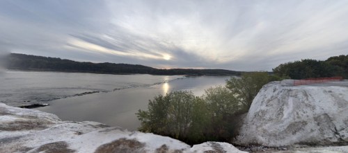 A serene river scene at sunset, with soft clouds and trees lining the banks, reflecting on the water's surface.