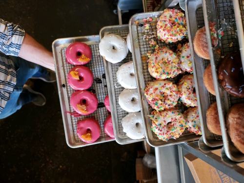 A top-down view of trays filled with colorful donuts, including pink, white, and sprinkled varieties.