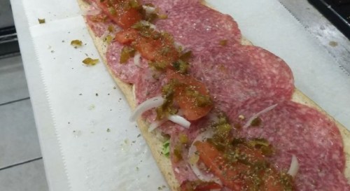 A long sandwich with layers of salami, tomatoes, onions, and green peppers on a white sub roll.