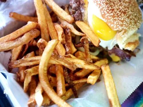 A close-up of a sesame seed bun burger with a runny egg, accompanied by a generous serving of golden fries.