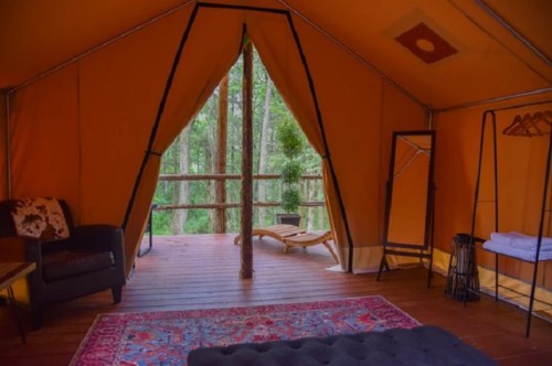 Cozy glamping tent interior with a view of trees, featuring a sofa, mirror, and a wooden deck.
