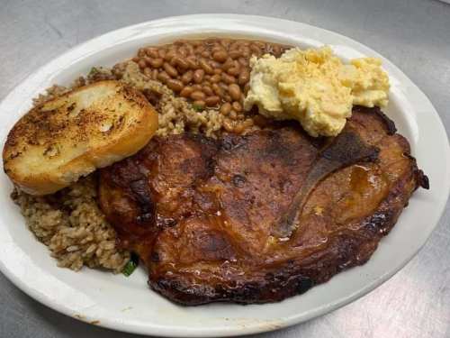 A plate of food featuring a grilled steak, rice, baked beans, a slice of toasted bread, and mashed potatoes.