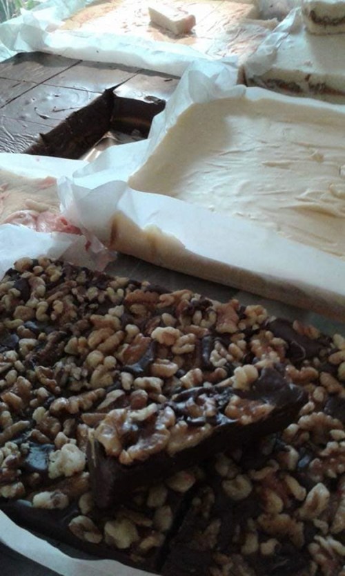 A variety of homemade desserts, including fudge and layered treats, topped with nuts on a parchment-lined surface.