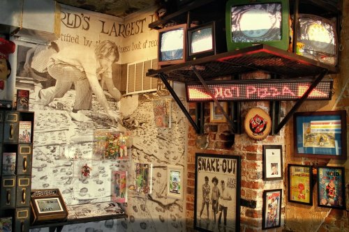 A quirky room filled with vintage TVs, posters, and memorabilia, featuring a large mural and eclectic decor.