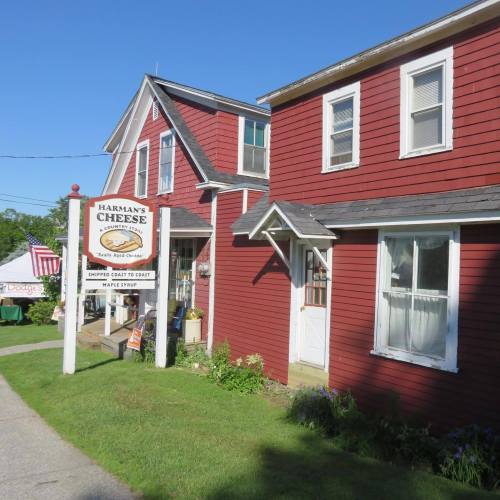 A red building with a sign reading "Harman's Cheese" and a white porch, surrounded by greenery and a clear blue sky.