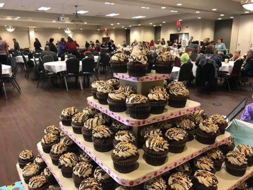 A tiered display of cupcakes with chocolate frosting and drizzled caramel, with a crowd in the background.